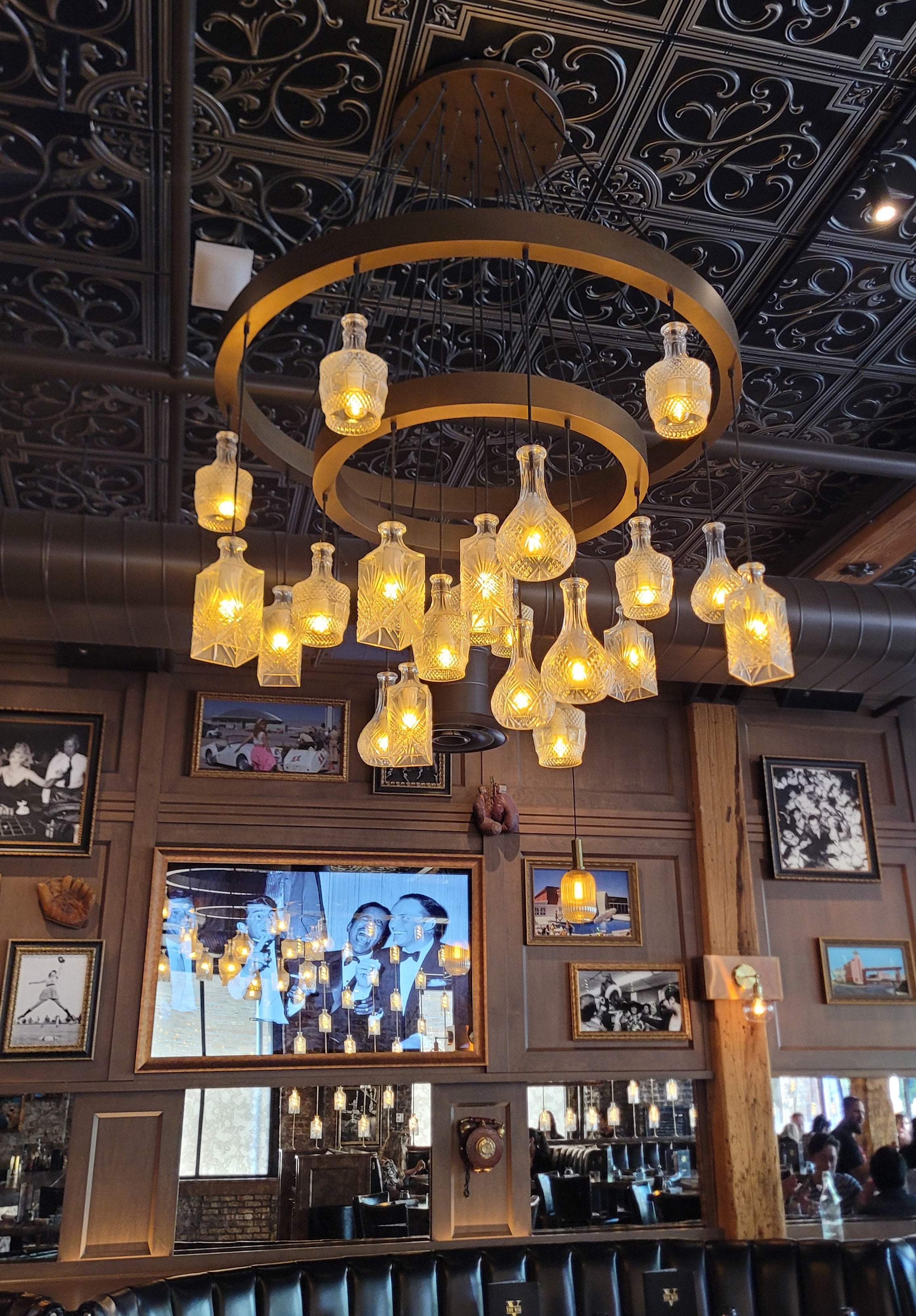 glass decanter whiskey bottle chandelier hanging in a room with decorative walls and framed pictures.