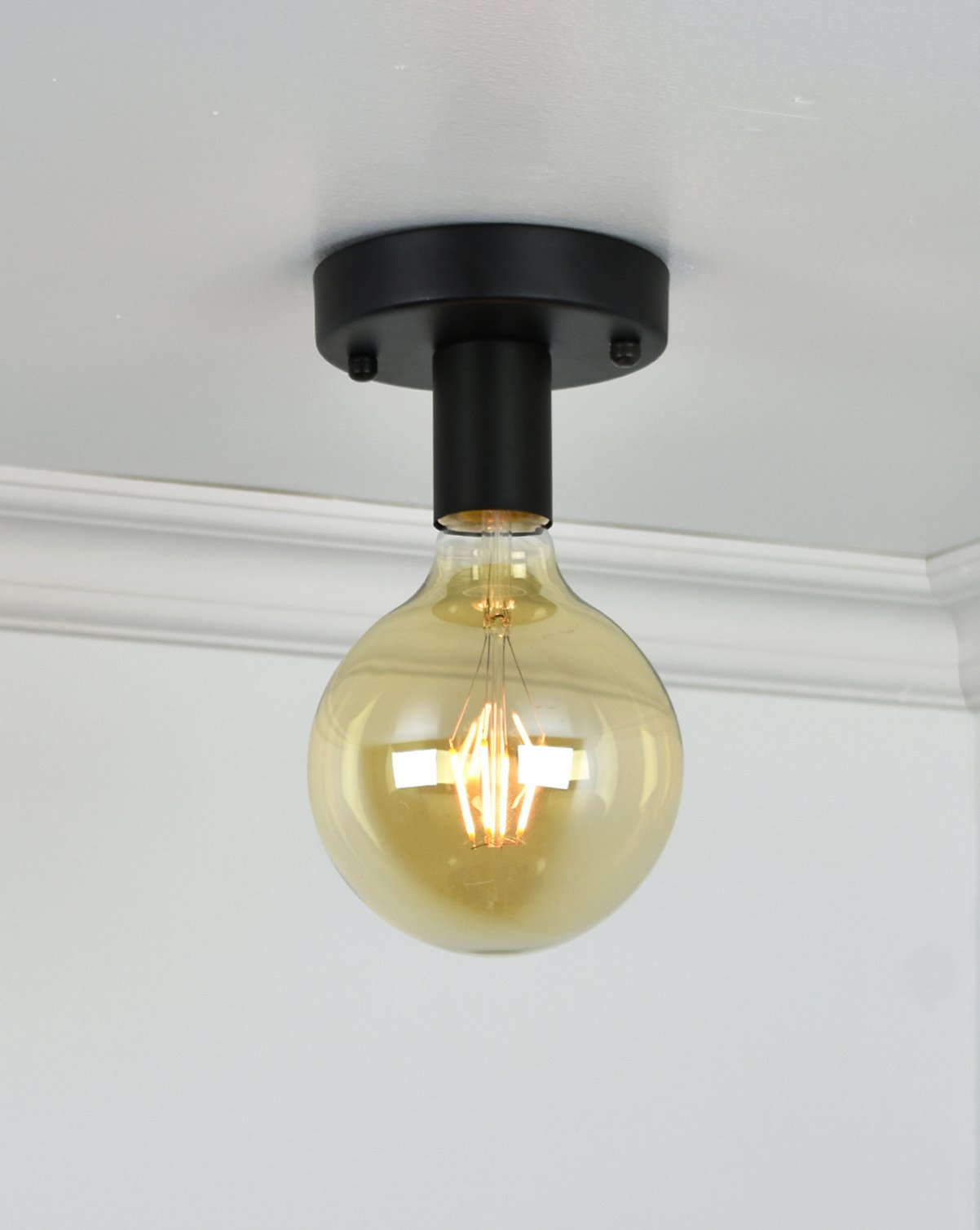 Flush mount light fixture with a black base and a large, round exposed bulb installed on a ceiling.