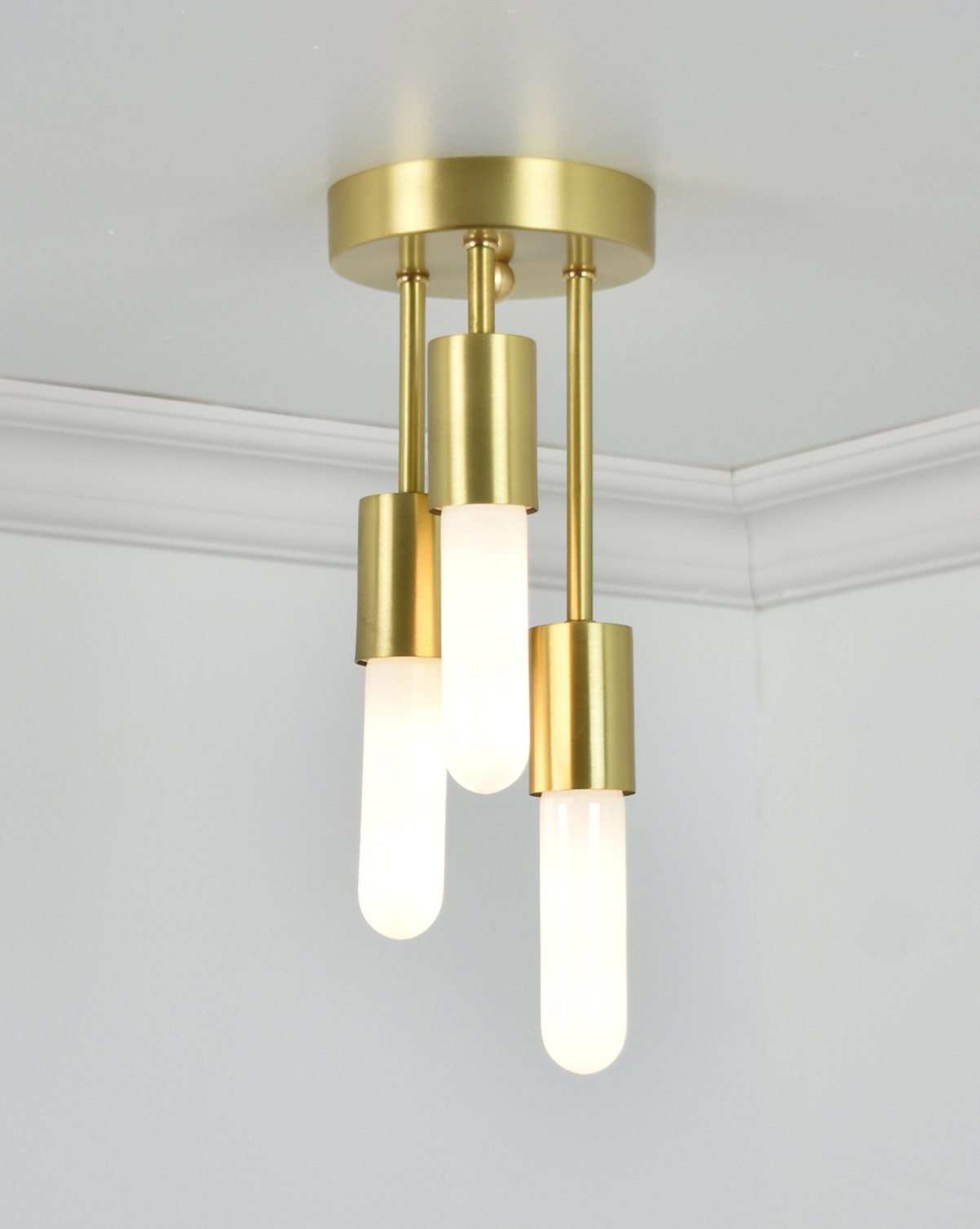 Semi-flush mount light fixture with a brushed brass base and three hanging bulbs with matching brass cylindrical housings.