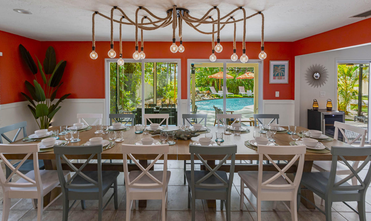 Dining room with a large table set for dinner, chairs, and a view of a pool and garden. rope swag chandelier with clear globes