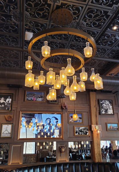 glass decanter whiskey bottle chandelier hanging in a room with decorative walls and framed pictures.