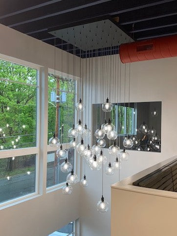 Modern chandelier hanging in a 2 story stairway foyer with large square base chandelier and hanging globe pendants