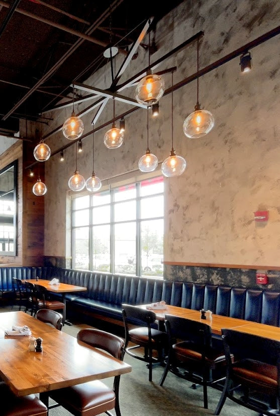 Restaurant interior with wooden tables, chairs, and hanging light bulbs. Large oversized chandelier