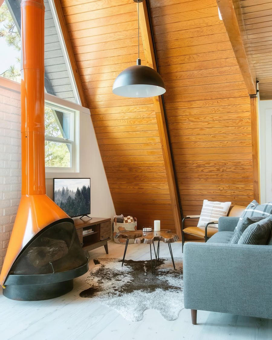Modern living room with a large orange fireplace, gray sofa, and wooden walls. Large dome shade