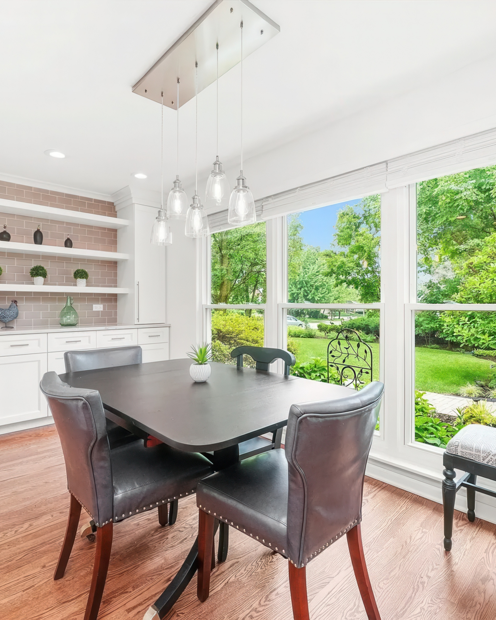 Dining room with a table and chairs near large windows with a view of greenery. modern glass small dining table lighting