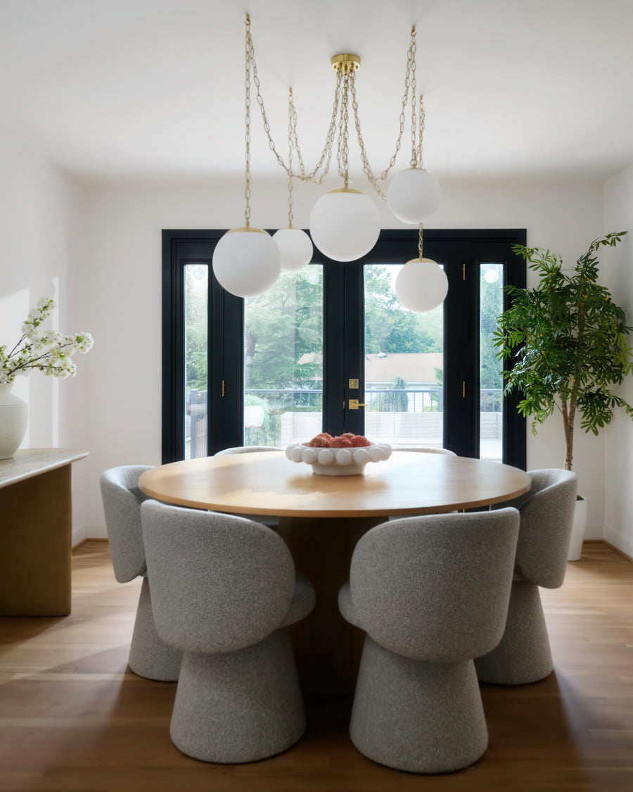 Dining room with a round wooden table and gray chairs, featuring a chandelier and large windows. brass chandelier 