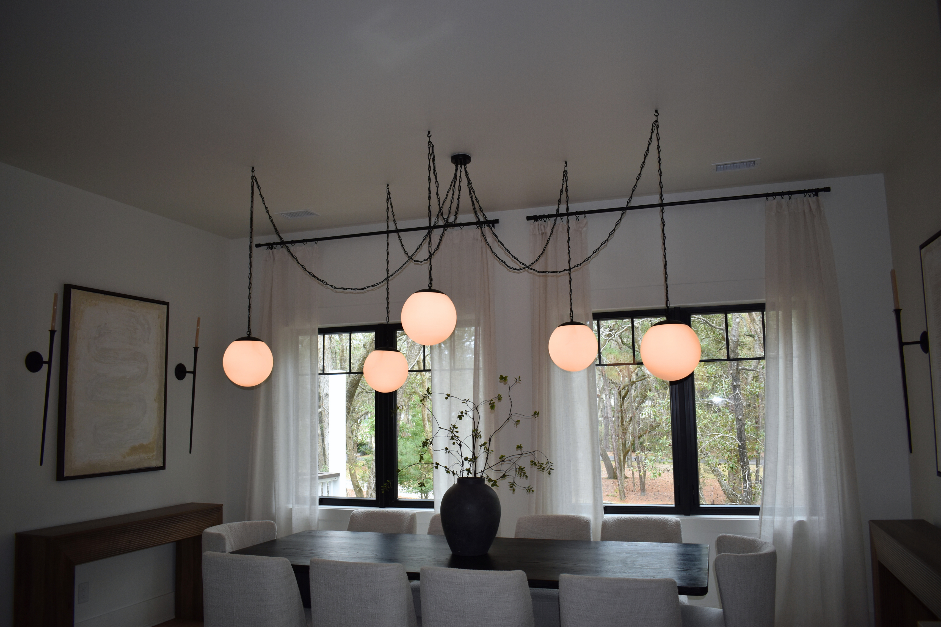 chain swag chandelier over soft modern dining room table glowing globe lighting